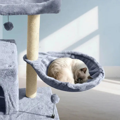 Cat resting in a gray hammock attached to a cat tree with a light blue wall in the background