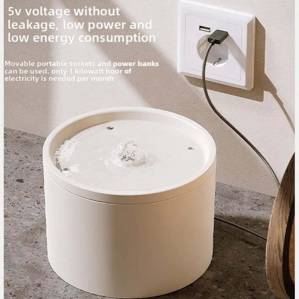 White cylindrical water fountain with power cord plugged into a wall usb socket, on a concrete floor