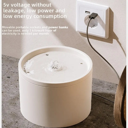 White cylindrical water fountain with power cord plugged into a wall usb socket, on a concrete floor